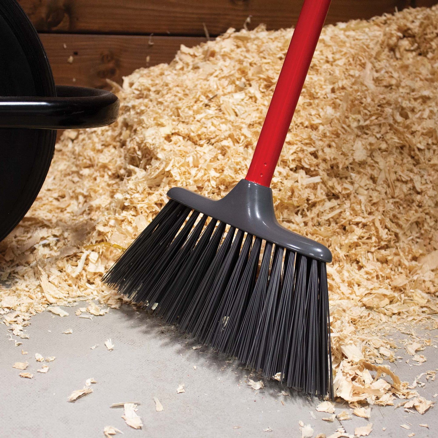 Poly Yard Broom with Red Handle sweeping up some shavings in a stable